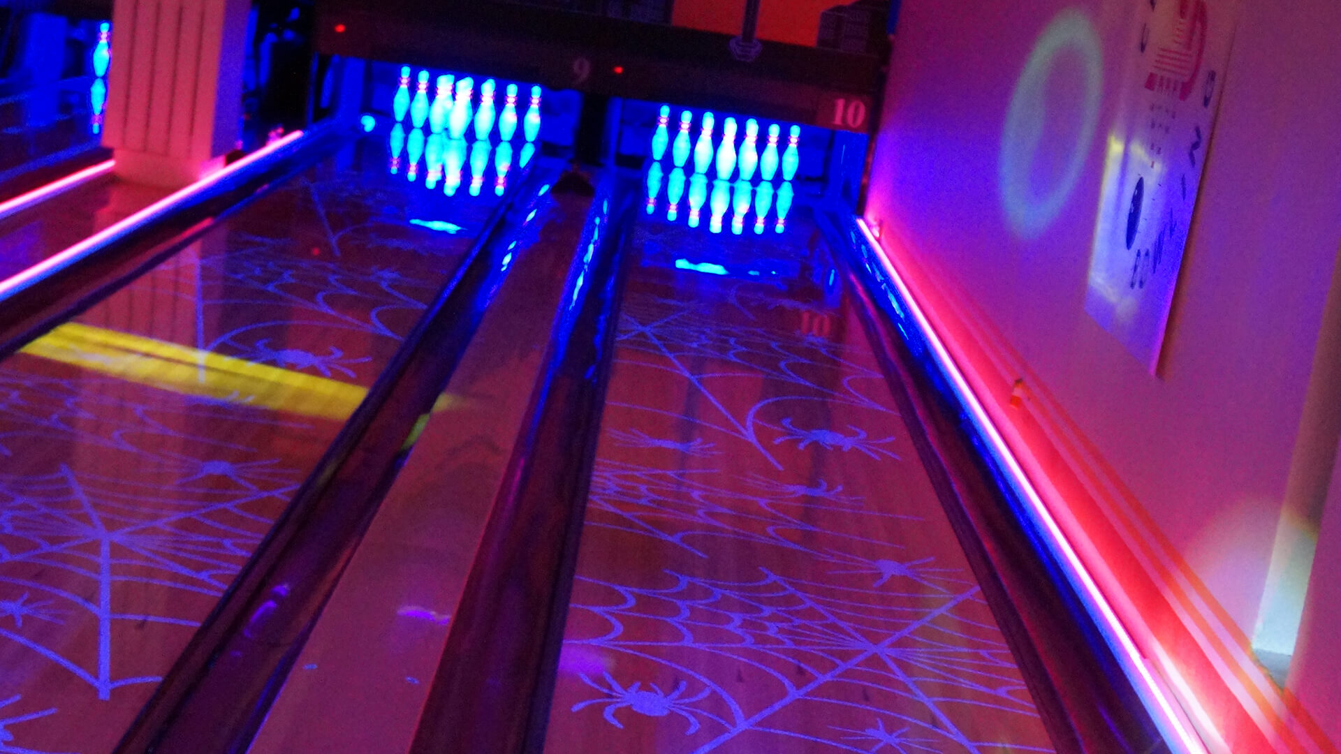 Discobowling close-up — blacklight-aktivert edderkoppspinn-grafikk lyser cyan og lilla på banen